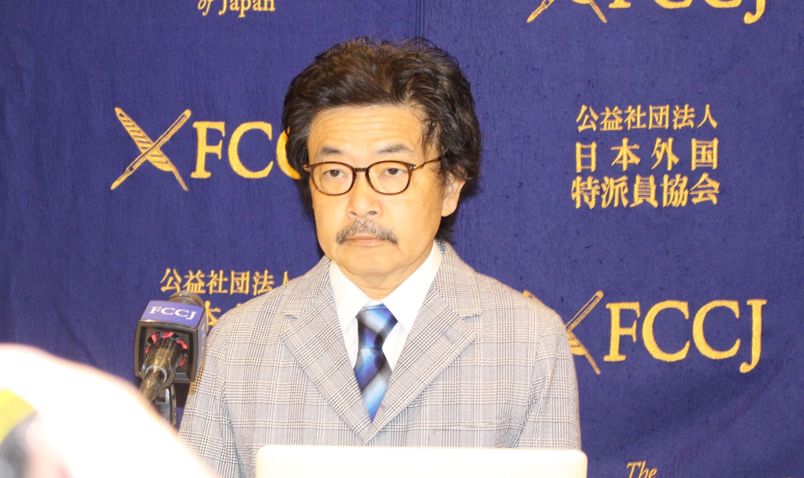 園子温氏　紺色チェックのジャケット／青チェックのネクタイを身に付けている